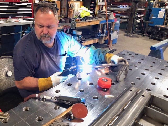 SMF shop employee welding on metal table